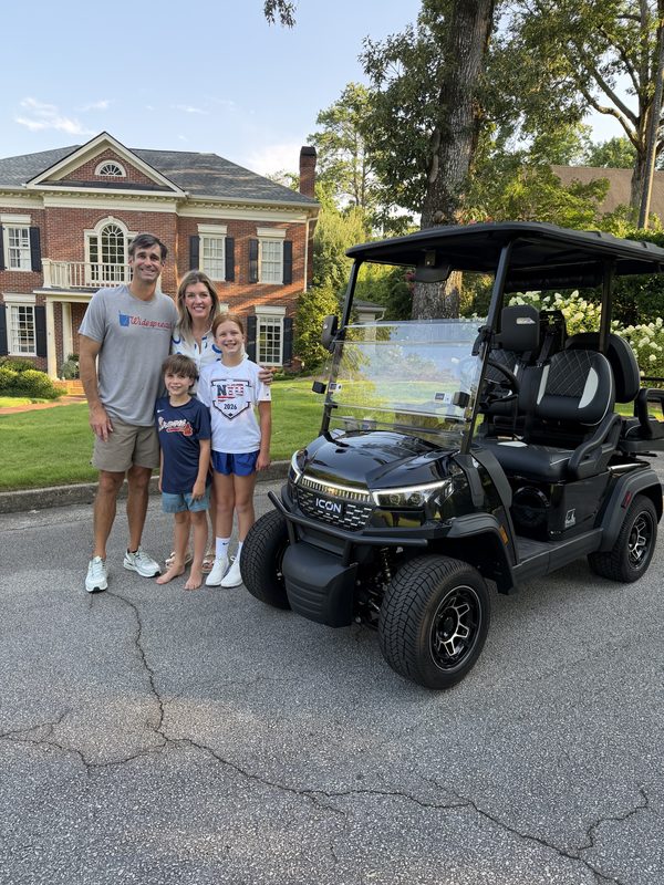 A family of four standing beside their new black six-seat lifted golf cart in the driveway of their home