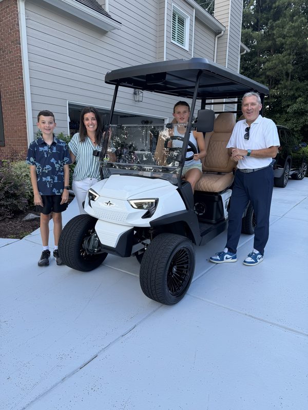 A family with a Prime Golf Carts team member beside a new white lifted golf cart on delivery day