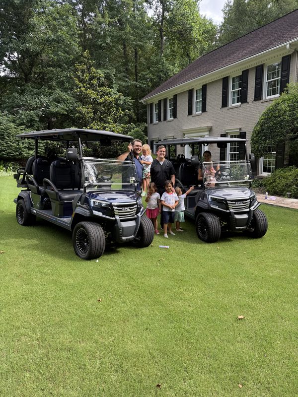 A family gathered around two new black lifted golf carts on the front lawn of their house