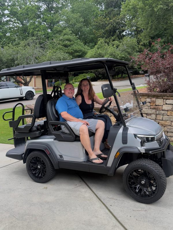 A couple sitting together in their new silver lifted golf cart in a driveway