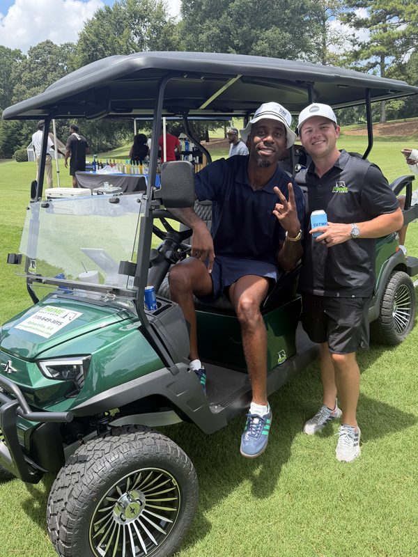 Two men with a new green lifted golf cart on a golf course