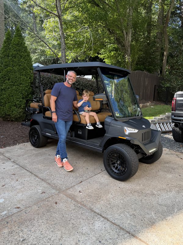 A man holding a toddler beside their new black lifted golf cart in a driveway
