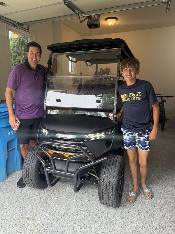 A father and son standing beside their new black golf cart in the garage