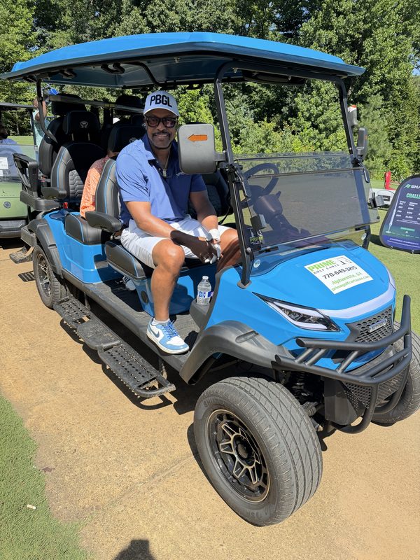 A man seated in a bright blue six-seat lifted golf cart parked on grass