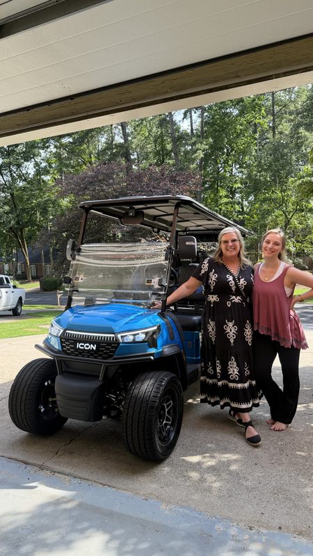 Two women standing beside a new blue ICON lifted golf cart in a garage