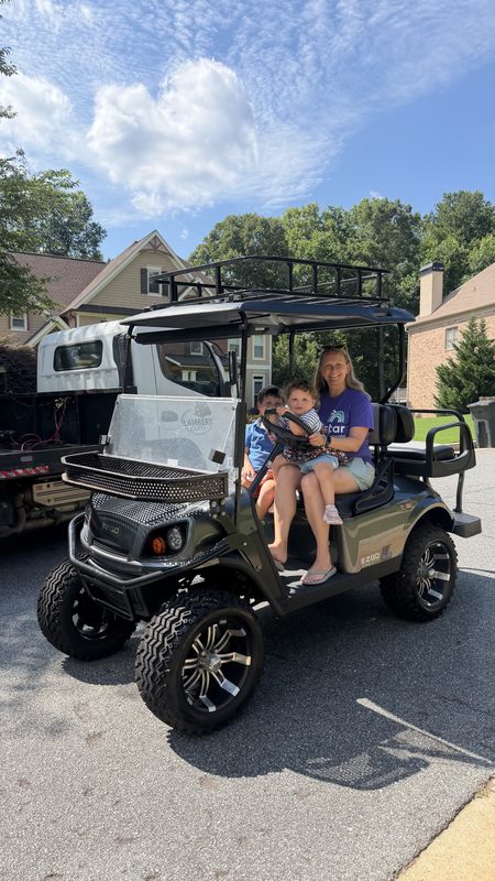 A woman and children sitting in a white lifted golf cart in a driveway