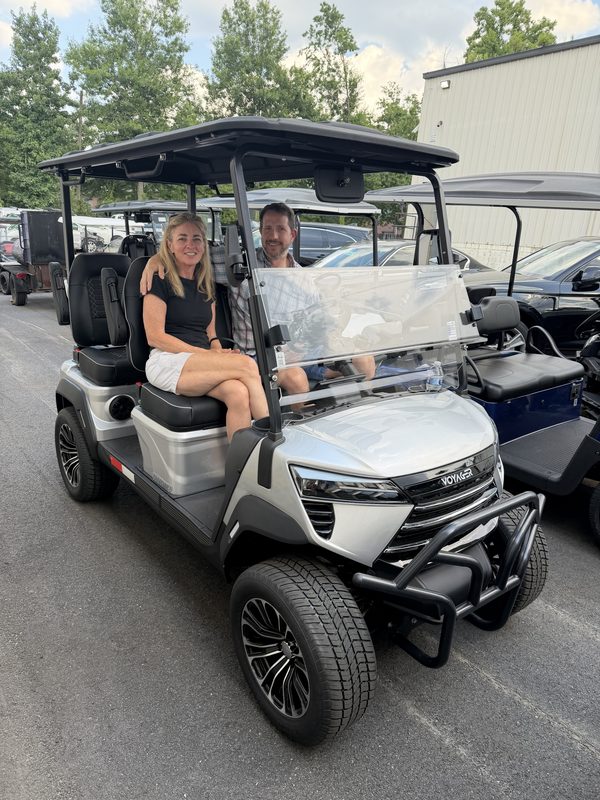 A couple seated in a new white lifted golf cart at the Prime Golf Carts showroom