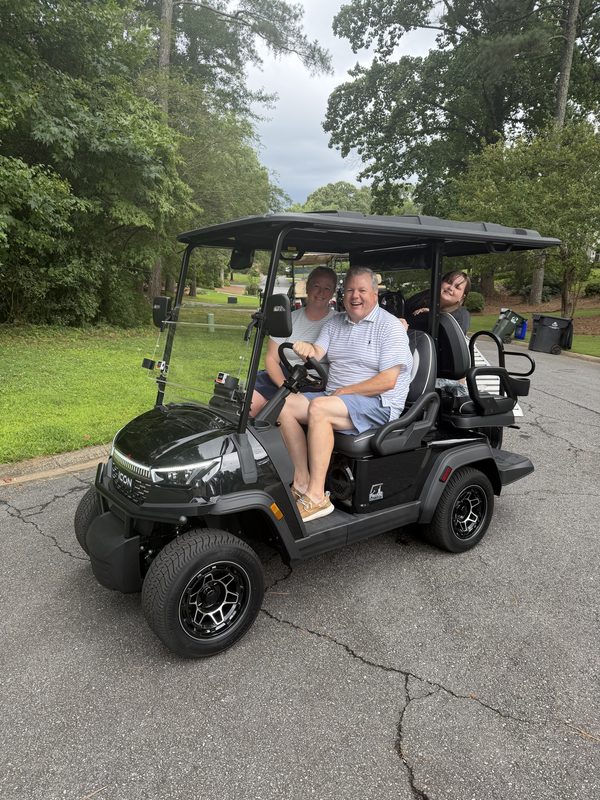 A couple sitting in their new black lifted golf cart in a driveway