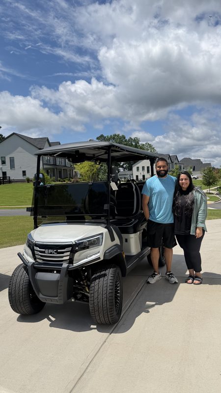 A couple standing beside their new black and white lifted golf cart in a driveway