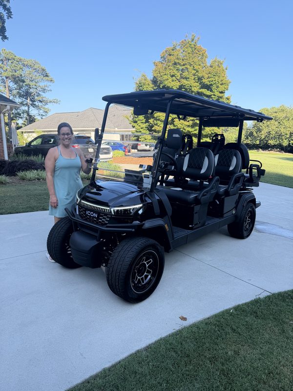 A woman standing beside a new black six-seat lifted golf cart in a driveway