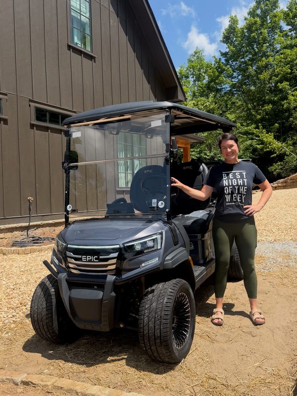 A woman standing beside her new black EPIC lifted golf cart on a gravel driveway