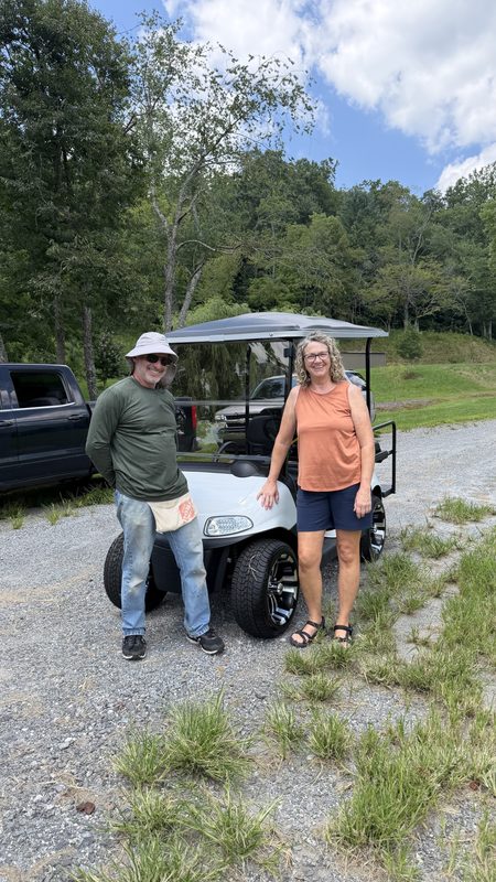 A man and a woman beside their new white golf cart on a gravel driveway