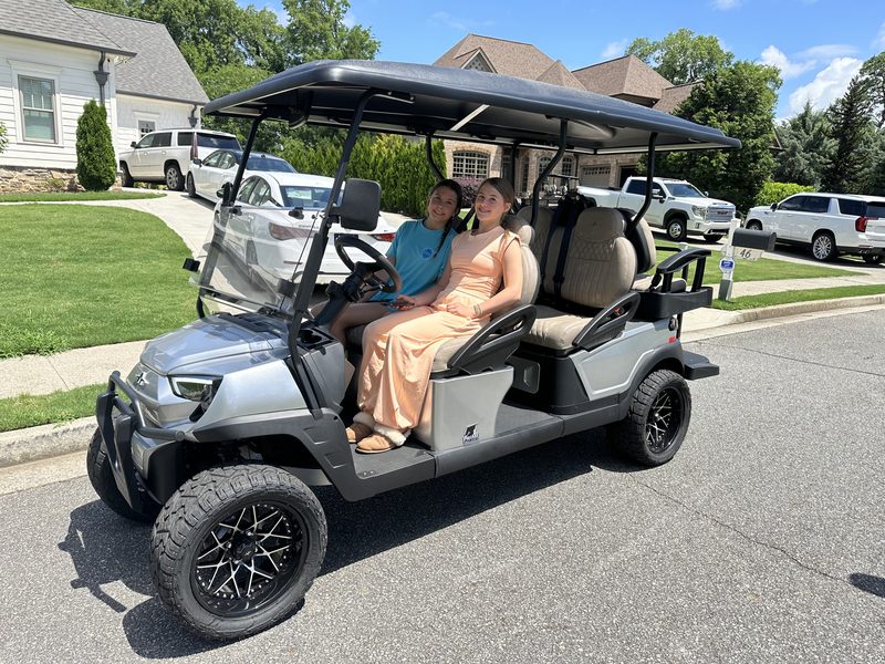 Two people seated in a silver six-seat lifted golf cart on a residential street