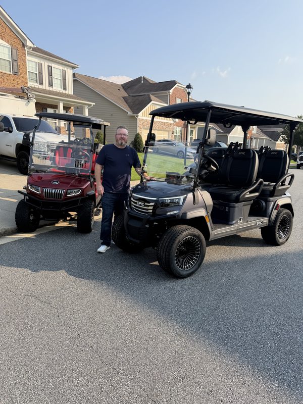 A man standing between a maroon golf cart and a new black lifted golf cart in a driveway