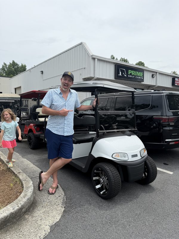 A man and a young child beside a white golf cart at the Prime Golf Carts showroom