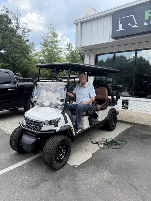 A man seated in a new white golf cart with tan seats outside the showroom