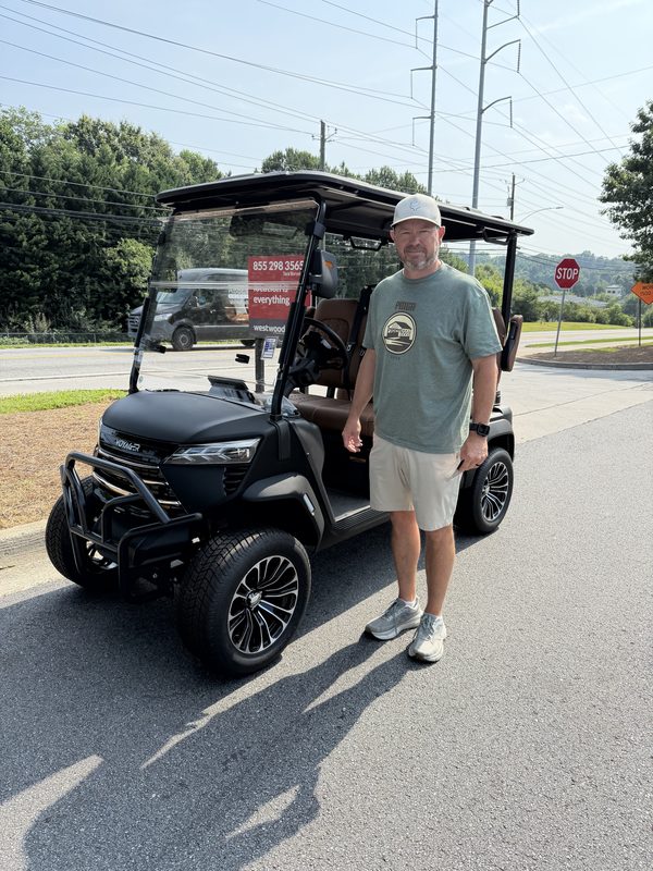 A man in a cap standing beside his new black lifted golf cart