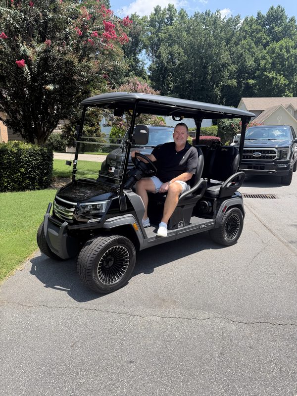 A man seated in his new black lifted golf cart in a driveway