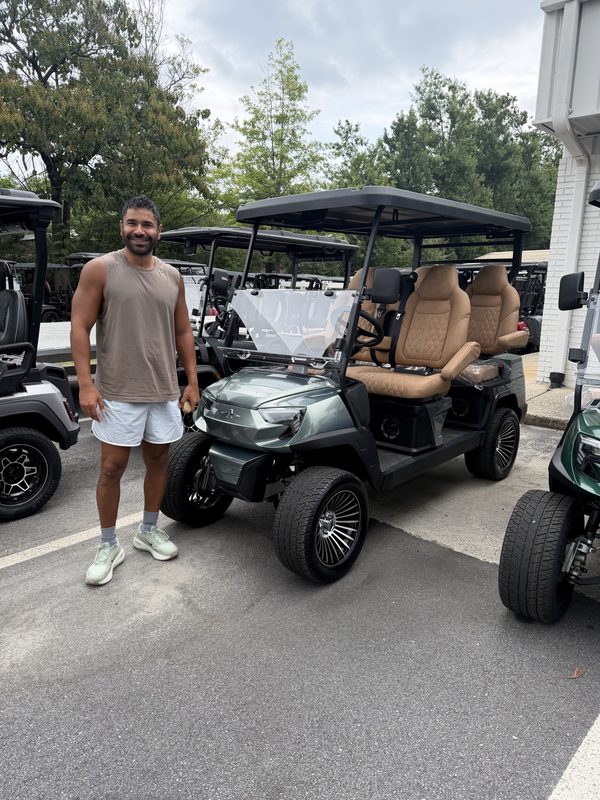 A man standing beside a row of new golf carts including a green lifted model