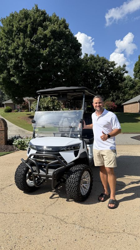 A man standing beside his new white lifted golf cart in a driveway