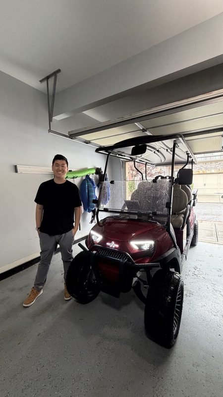 A man standing beside his new burgundy golf cart parked in a garage