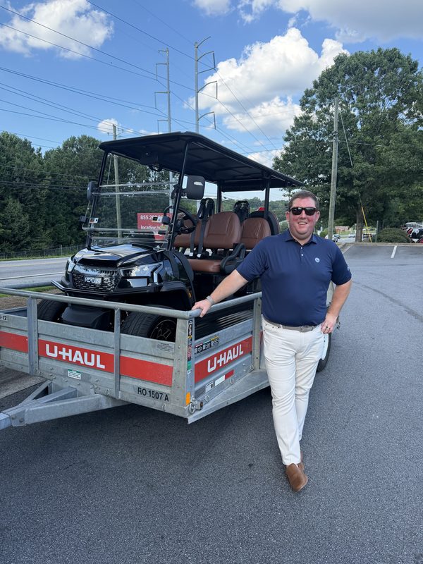 A man beside a new black golf cart loaded on a trailer ready for transport