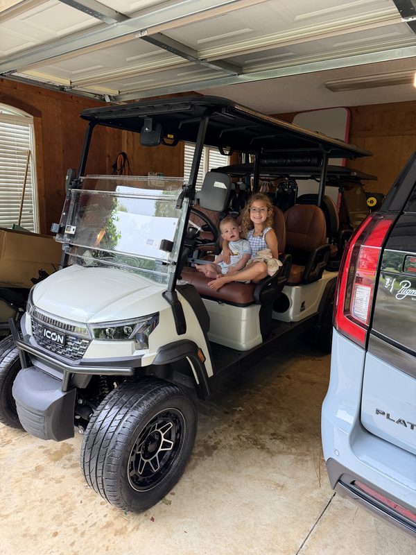 A child sitting in a new cream six-seat golf cart during delivery