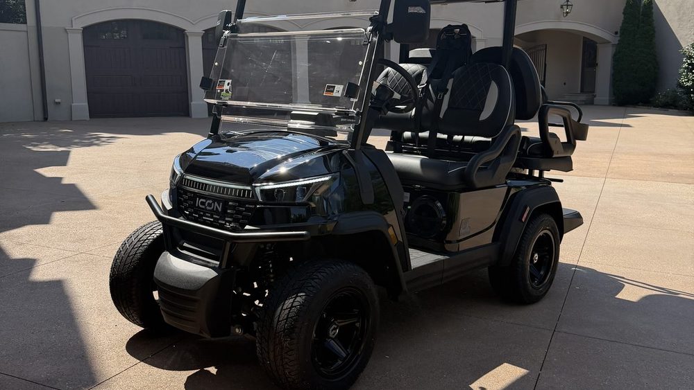 A black four-passenger lifted ICON golf cart parked in a residential driveway