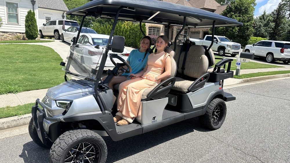 A silver six-passenger lifted golf cart with three rows of seats on a residential street